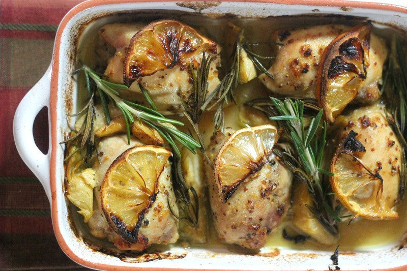Dish of chicken thighs baked with HANAH Vechur Ghee, garnished with lemons and rosemary