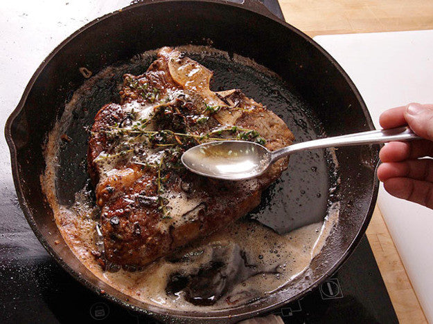 Spoon basting a steak and thyme with HANAH Vechur Ghee in a cast iron skillet