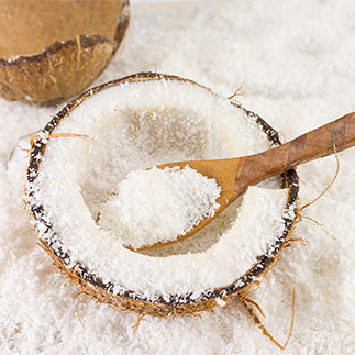 Spoon of coconut flakes surrounded by scattered coconut flakes in a coconut bowl