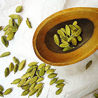 Scattered green cardamom pods on a table and in a wooden bowl