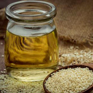 Clear jar of sesame oil surrounded by scattered sesame seeds